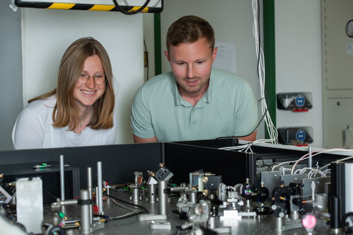 Two scientists in front of an optical table with mirrors and lasers